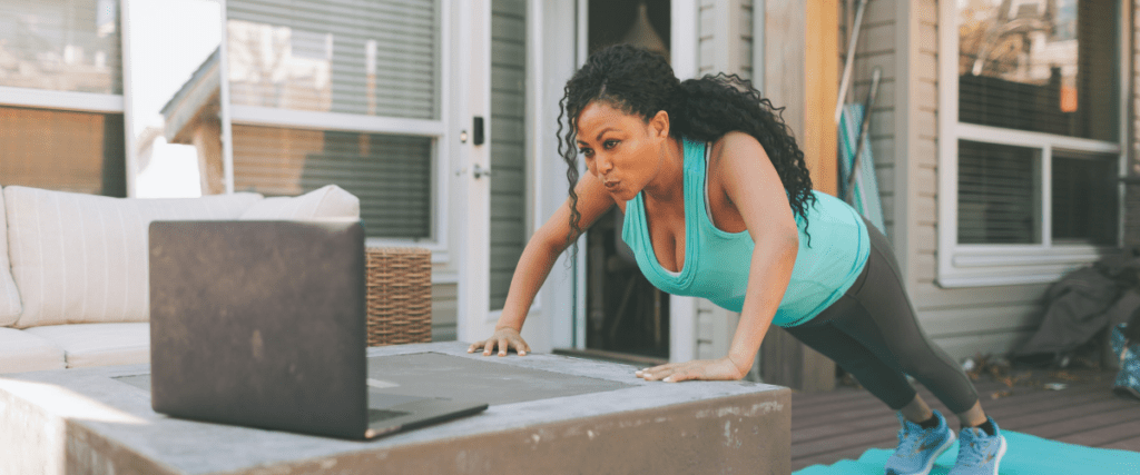 Woman doing pushups on her porch while watching her computer for a workout. 