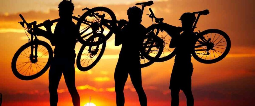 Three cyclist holding up their bike in the sunset. 