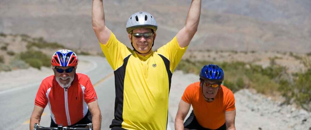 3 older men in full cycling outfits smiling into the camera. 