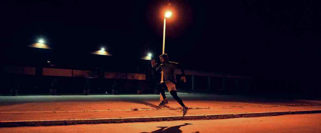Man running in street next to street lamp at night. 