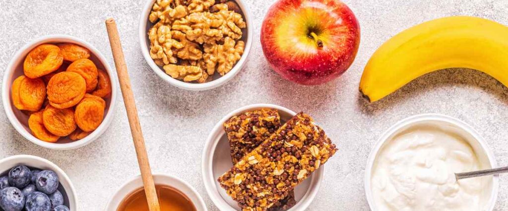 View of close up of healthy snack options like yogurt, bananas, applies, and granola bars.