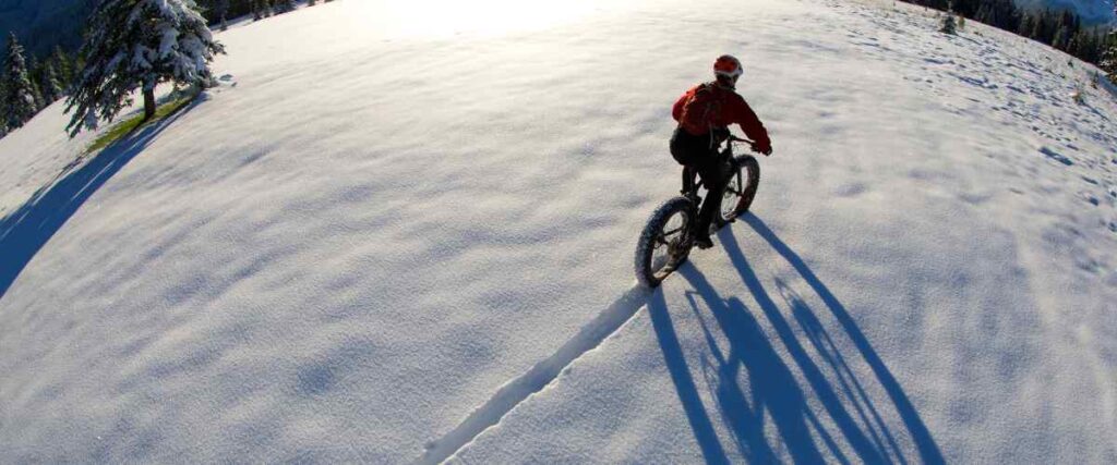 Aerial view of a cyclists on his bike from behind going thru the snow. 