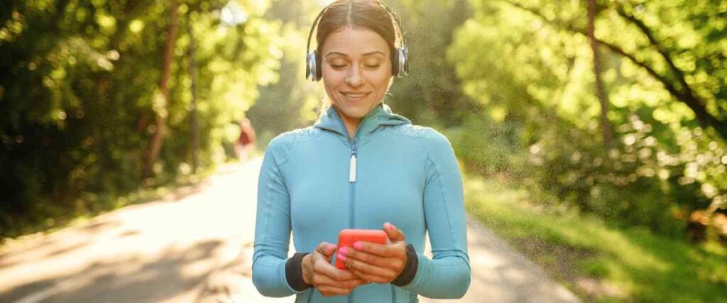Woman about to go on a run looking down on her phone picking a podcast. 