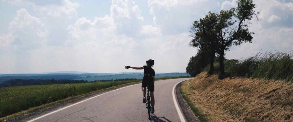 A cyclists on a clear road making a signal she is turning left. 